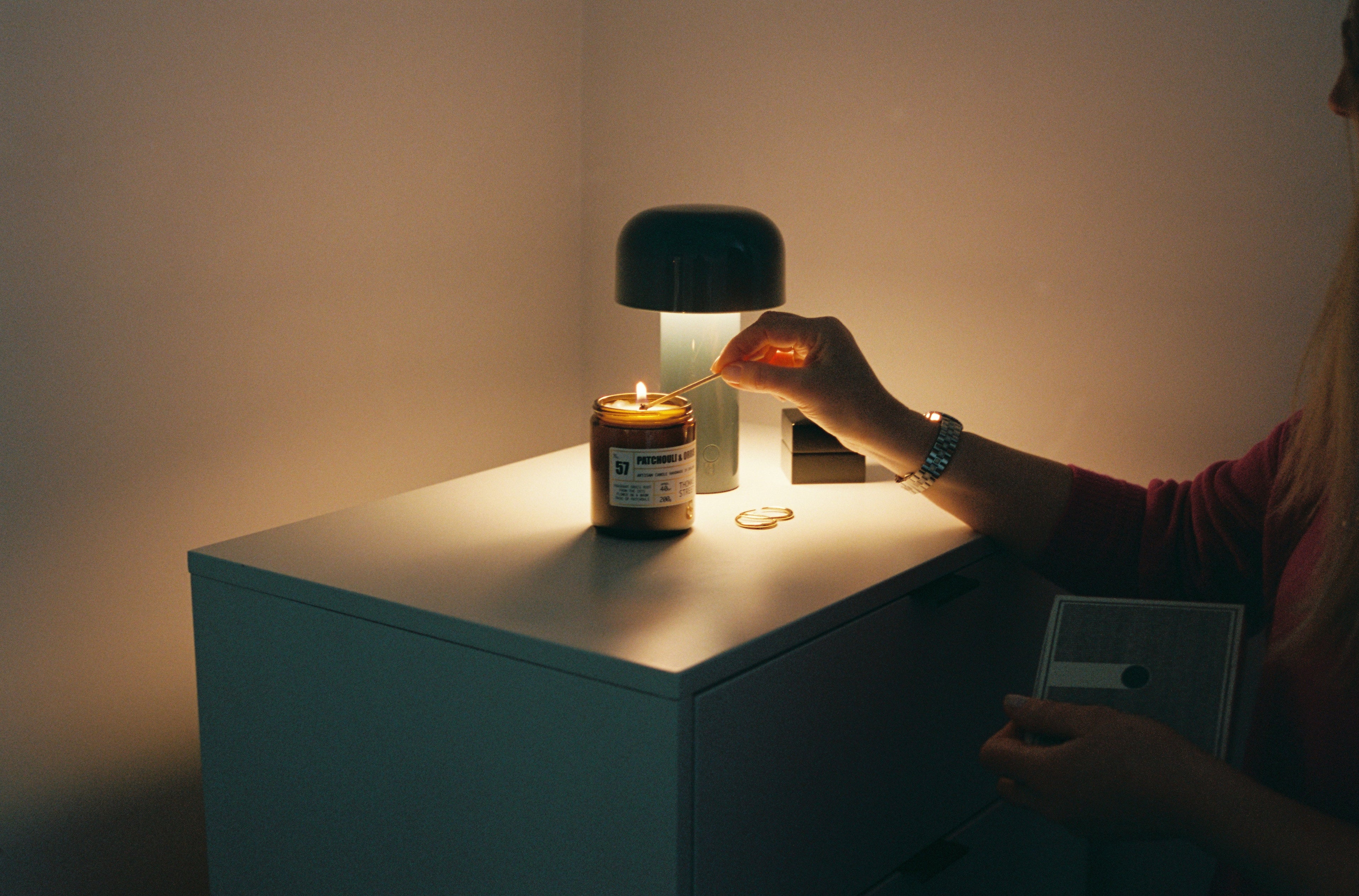 Thomas Street Patchouli Orris candle being lit by a matchstick in an urban apartment